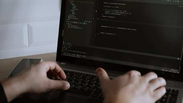 Men's hands press the keys of a laptop keyboard. A man writes a program. The developer is coding. The program code is visible on the screen. Work at home
