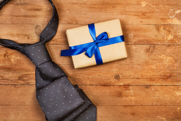 Caja de regalo con un lazo azul junto a una corbata sobre un fondo de madera rústico. Vista...