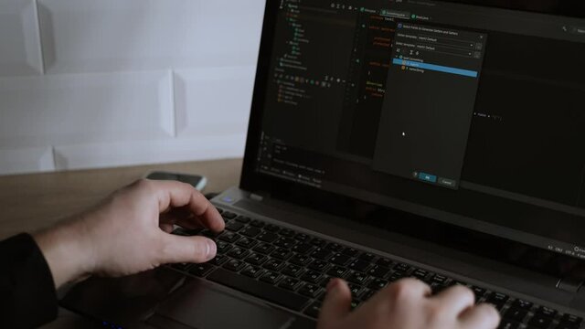 Men's hands press the keys of a laptop keyboard. A man writes a program. The developer is coding. The program code is visible on the screen. Work at home