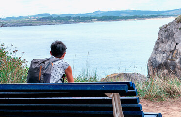 woman with backpack sitting on a bench looking at the sea