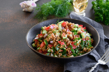Cooked whole grain cereal spelt as salad with vegetables, tomatoes, cucumber, greens.