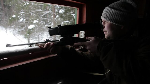 A hunter with a gun on an observation tower for hunting in the forest. A man hunts wild animals from a tower, prepares to shoot with a carbine, looks into the scope and waits for prey
