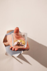 The hand holds a glass of tablets and pills breaks through a hole in the paper. Art concept of drugs, treatment. Copy space