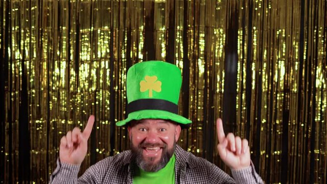 a man with a beard wearing a large green hat celebrates st patrick's day, points to blank space for text.