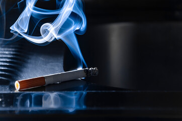 Close-up of a cigarette with a beautiful plume of smoke. not extinguished cigarette on a dark...