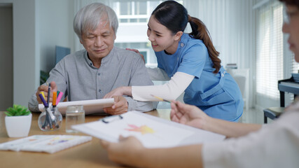 Attractive young senior asian citizen couple sit at home watercolor painting artwork on desk table with nurse feeling happy in mental health therapy or asia older people quarantine activity lifestyle.