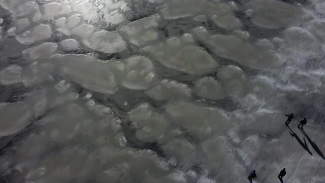 Ice skating people on a frozen lake during a beautiful winter day in The Netherlands. Aerial drone point of view.