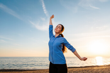 Portrait of a young smiling woman in sportswear is warming up on the beach. The concept of outdoor sports. Wellness