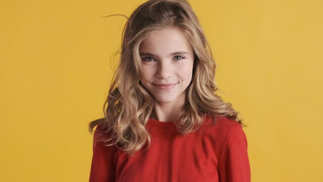 Pretty blond teenager girl dressed in red sweater dancing and smiling on camera over colorful background