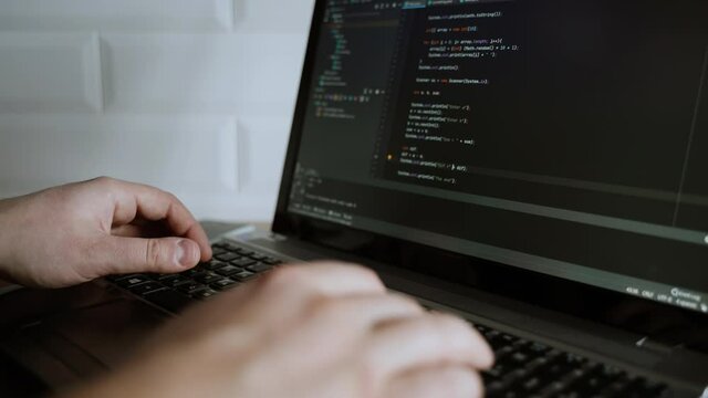 Men's hands press the keys of a laptop keyboard. A man writes a program. The developer is coding. The program code is visible on the screen. Work at home