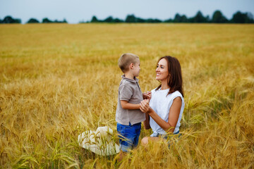 Happy family of mother and son in a summer wheat field. A young woman with a boy in nature.