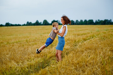 A happy family of mother and son in a summer wheat field. A woman holds her son in her arms and circles.
