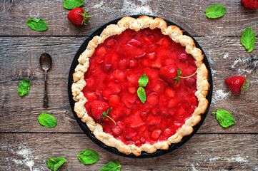 Homemade strawberry tart with cream cheese and mint on wooden background. 