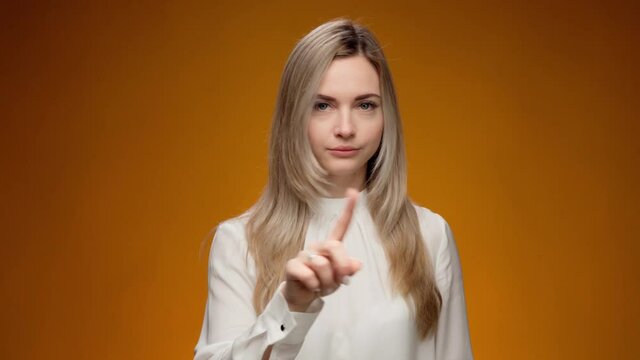 Young woman wags a finger, rejecting something, against yellow background