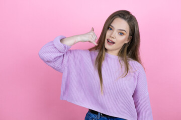 Young pretty woman with long hair standing over isolated pink background smiling doing phone gesture with hand and fingers like talking on the telephone