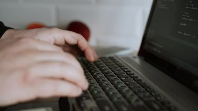 Men's hands press the keys of a laptop keyboard. A man writes a program. The developer is coding. The program code is visible on the screen. Work at home
