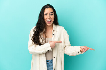 Young caucasian woman isolated on blue background surprised and pointing side