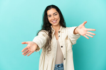 Young caucasian woman isolated on blue background presenting and inviting to come with hand
