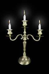 Fototapeta na wymiar Triple bronze candelabrum with three burning candles on black background