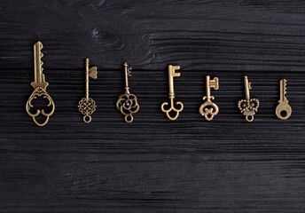 varied, small decorative keys lie in a row on a black wooden background. The concept of the...