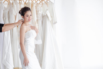 Beautiful Asian bride happy with bridesmaids together help each other to fit elegant lace dress, wedding dress maker try to fit the bride suit in wedding studio or Wedding dress shop store