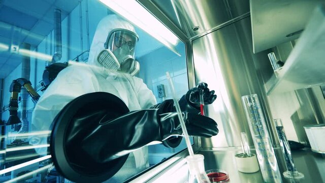 Specialist in a hazmat suit is using a laboratory cabinet testing probes