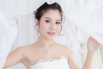 Beautiful Asian bride in elegant wedding dress having fun with camera snapshot smile and laughing, close up you happy woman in bridal dress post to take photo on wedding day in private room