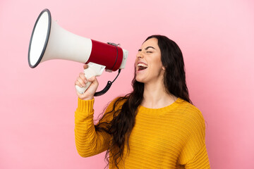 Young caucasian woman isolated on pink background shouting through a megaphone to announce something in lateral position