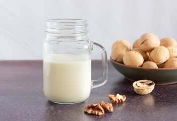 Vegetable walnut milk in a glass cup with a handle. Walnuts in a plate in the background. Healthy drinks, vegetarianism. Side view.