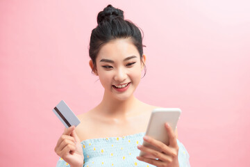 Image of emotional happy young pretty woman posing isolated over pink background using mobile phone holding credit card.