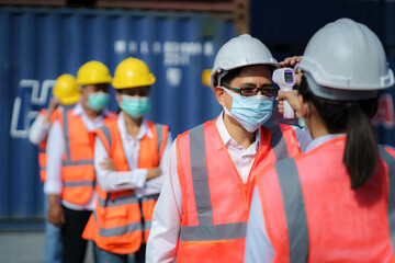 Asian woman foreman scanning fever temperature with digital thermometer to her staff worker wearing hygiene face mask protect from Coronavirus or COVID-19.