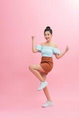Fototapeta na wymiar Portrait of an excited asian woman jumping and looking at camera isolated over pink background
