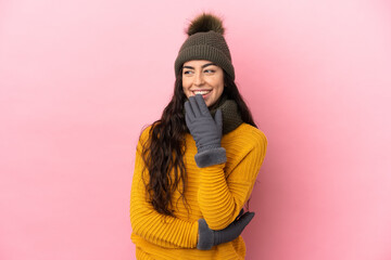 Young caucasian girl with winter hat isolated on purple background looking up while smiling