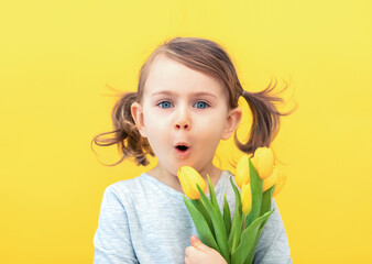 Easter, holidays, spring, mother's and father's day concept - happy, funny,smiling, little child girl in grey dress holds tulips posing isolated yellow background. Happy mothers day. Delivery flowers