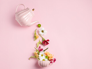 Creative layout with tea pot pouring fresh flowers and leaves into tea cup on pastel pink background. Creative floral spring bloom concept. Still life visual trend. Flat lay.