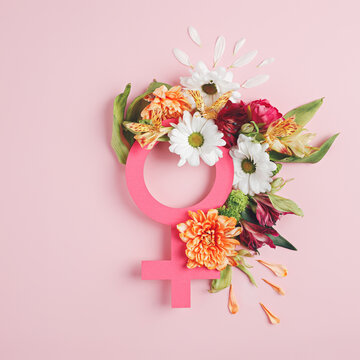 Female symbol with fresh spring flowers and leaves against pastel pink background. Creative Women's day or feminism concept. Gender equality visual trend. Flat lay. 