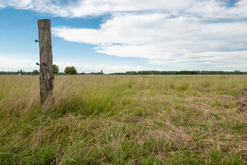 Zaunpfosten steht auf einem gr&uuml;nen Feld mit Blick &uuml;ber die bezaubernde Landschaft, blauer bew&ouml;lkter Himmel im Sp&auml;tsommer