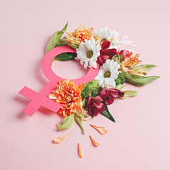Female symbol with fresh spring flowers and leaves against pastel pink background. Creative Women's day or feminism concept. Gender equality visual trend. Flat lay. 