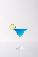 Blue alcoholic drink in cocktail glass with lime slice isolated on white and gray background
