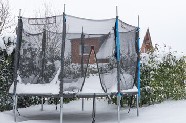 weathered trampoline with snow in a garden