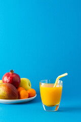 Delicious sweet orange or mango juice in glass and ripe fruits on a blue background