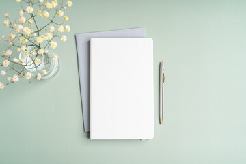 Top view blank paper Notebook, flowers, water with lemon and pen. Desktop mock up, Flat lay of green working table background with office equipment, mockup greeting card