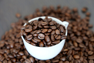 Coffee beans in white cup on dark wooden table. Dark and roasted coffee, concept of natural drink