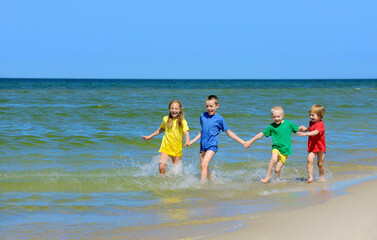 Two girls and two boys in colorful t-shirts running on sandy beach