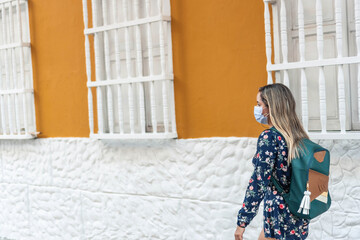 Outdoor portrait of a young Latina woman wearing a protective mask walking around the city during the coronavirus outbreak.