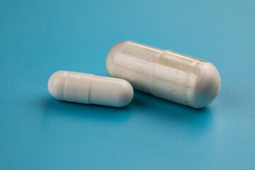 Two white pills capsule on blue background.