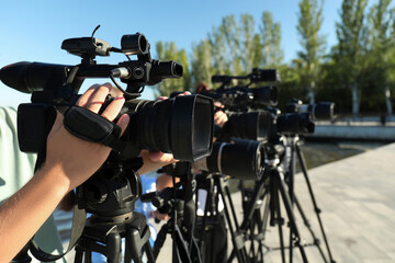 Operators with professional video cameras working outdoors on sunny day, closeup