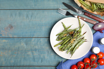 Delicious baked green beans served on light blue wooden table, flat lay. Space for text