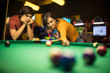 Young couple spending time in billiard room. Woman playing billiard.