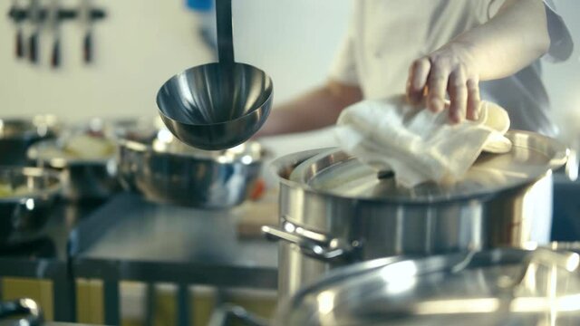 Two cooks in the kitchen are cutting cabbage and sweet peppers. The chef pours the ingredients into a pot of boiling water and stirs the soup with a ladle. Close up.